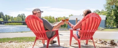 Two people sitting in lawn chairs with beverages looking out onto a lake