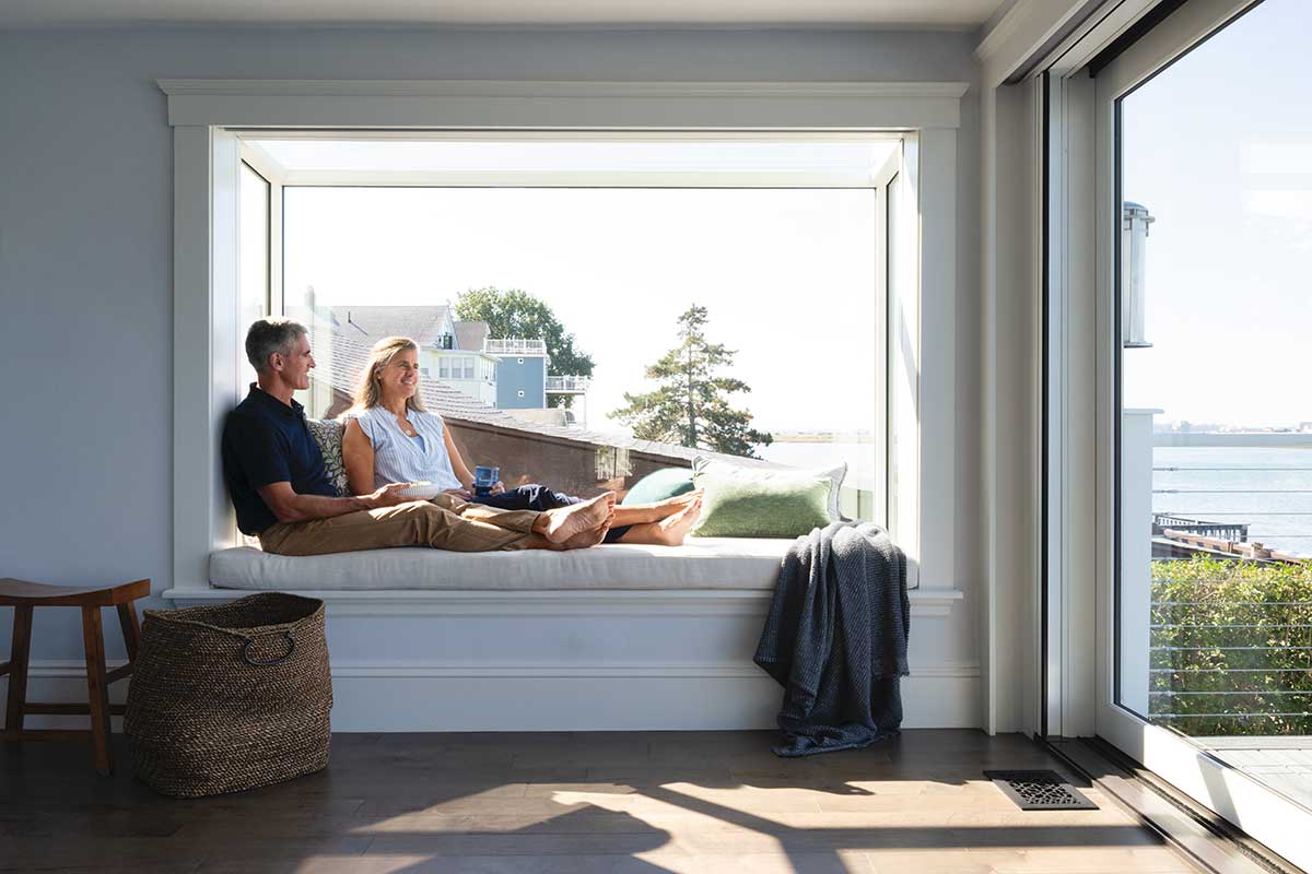 A man and woman sitting in a Marvin Skycove in a living room, next to a Marvin Modern Multi-Slide door.