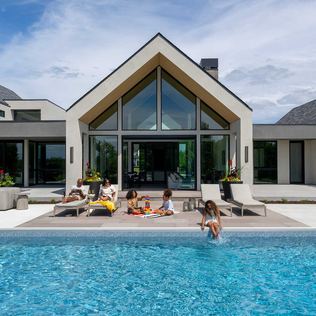 A family sitting by a pool behind a modern home, featuring Marvin Ultimate direct glaze windows.