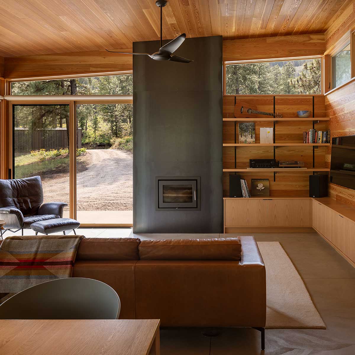 The family room of a mid-century modern home, featuring a tall fireplace, lots of wood, and Marvin Ultimate windows and doors.