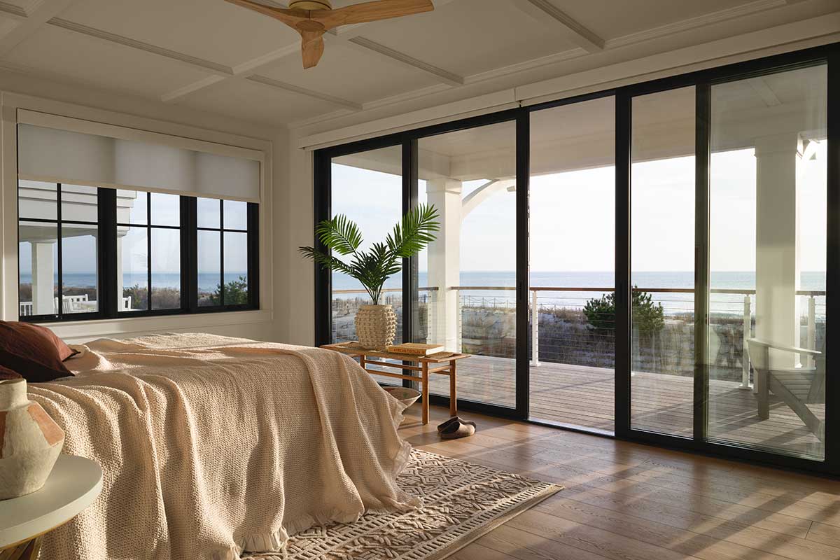 A bedroom in a contemporary home in Bethany Beach, Delaware, featuring a Marvin Modern Multi-Slide Door and an Elevate Casement window with a view of the ocean.