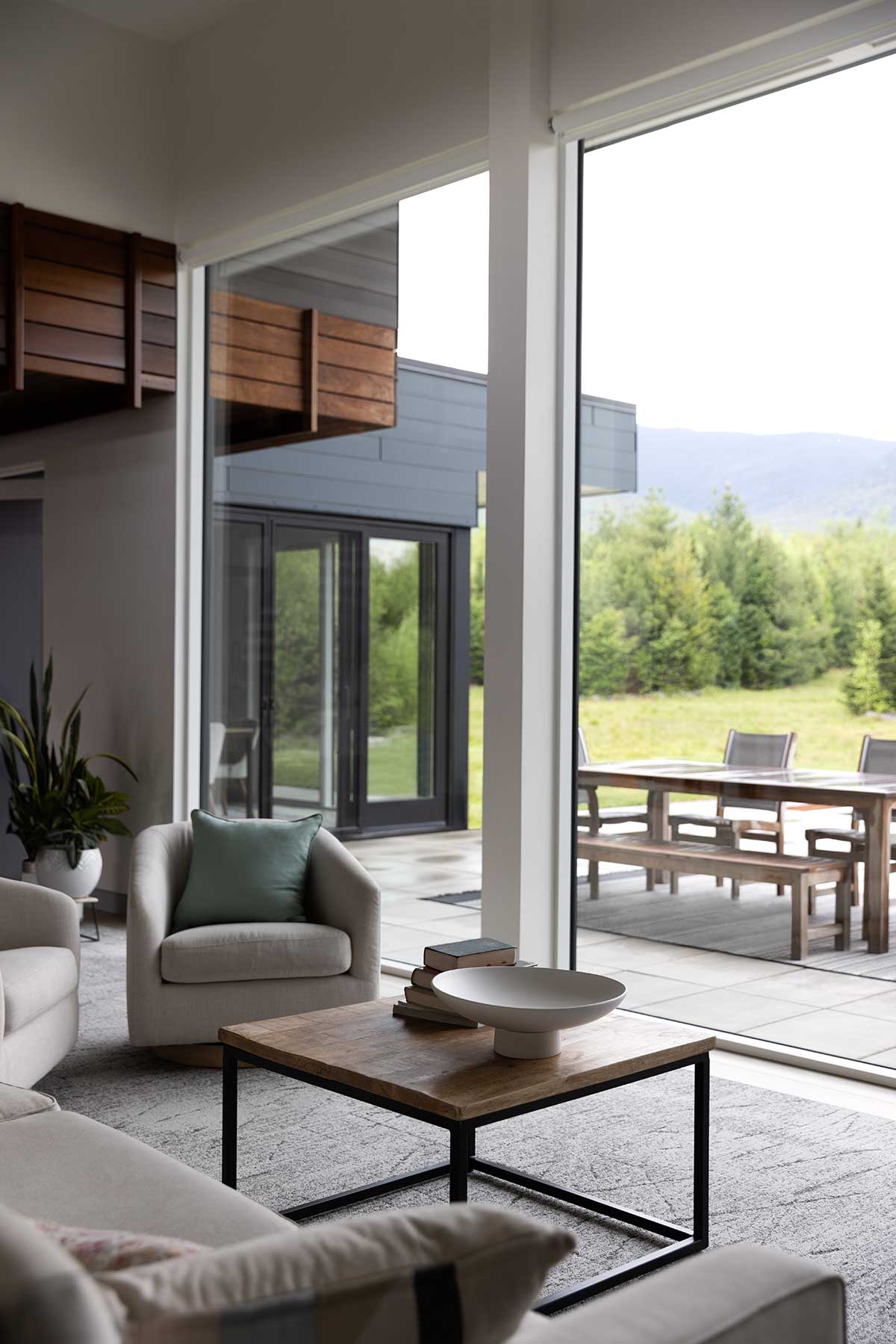 A modern living room with large Marvin Modern Direct Glaze windows looking out to a patio and mountains in New Hampshire.
