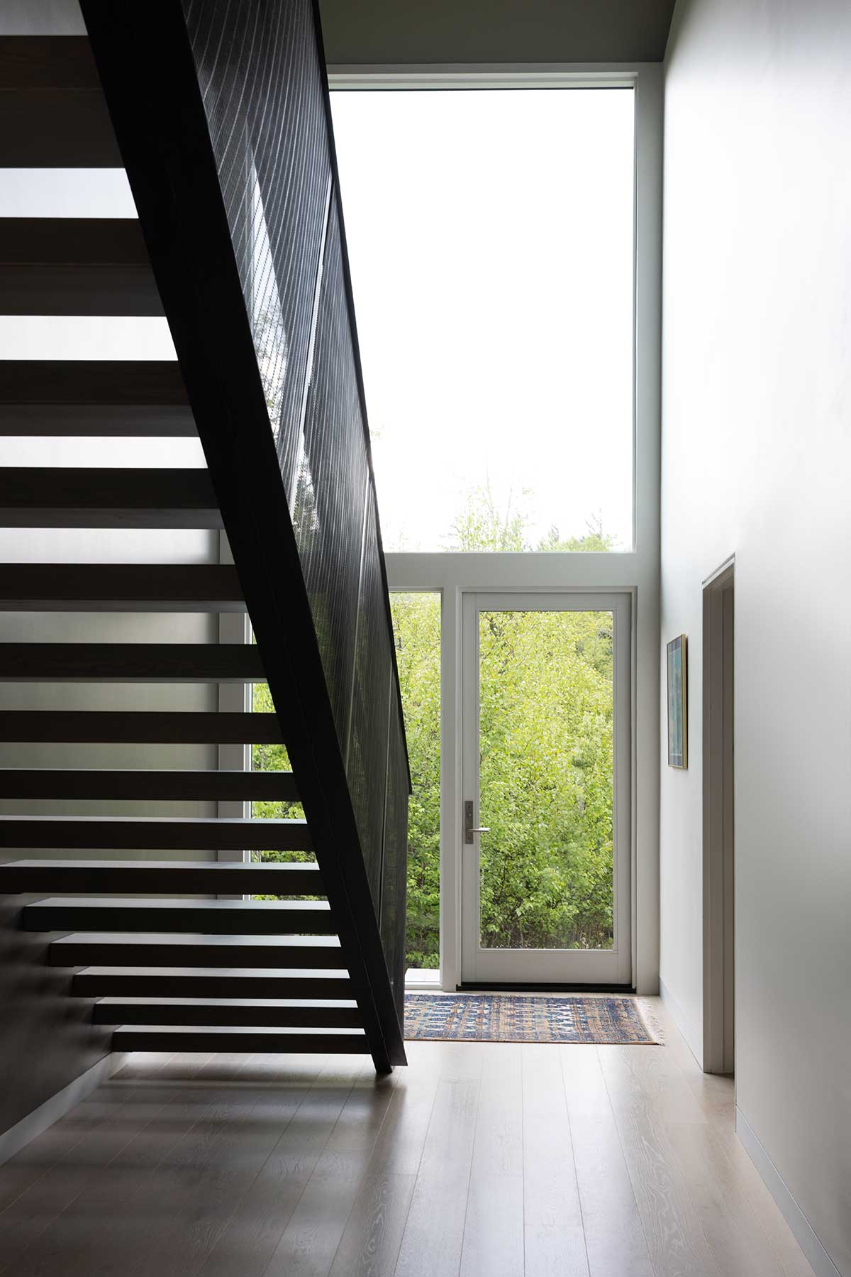 Underneath a staircase in a modern home, looking outside through a Marvin Modern Direct Glaze window and an Ultimate Outswing French Door.