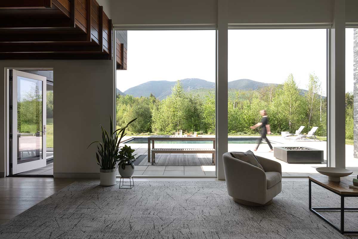 A modern living room looking out through Marvin Modern Direct Glaze windows to a pool deck with a person walking around it.