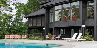 A resort-style pool with pink and white mid-century pool furniture against the backdrop of a black home in Minnesota with Marvin Essential windows.