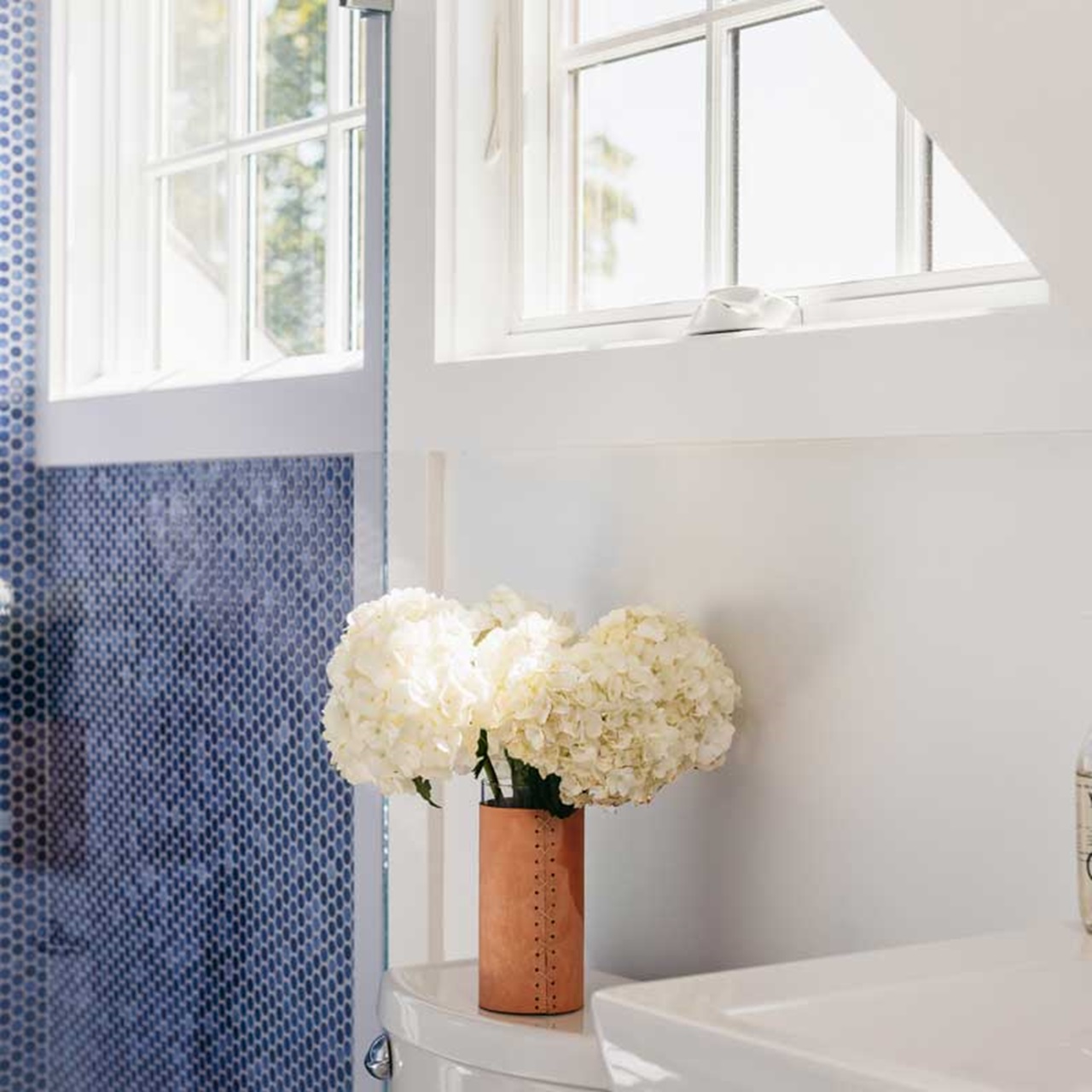 Bathroom with vase of flowers in front of two white awning windows