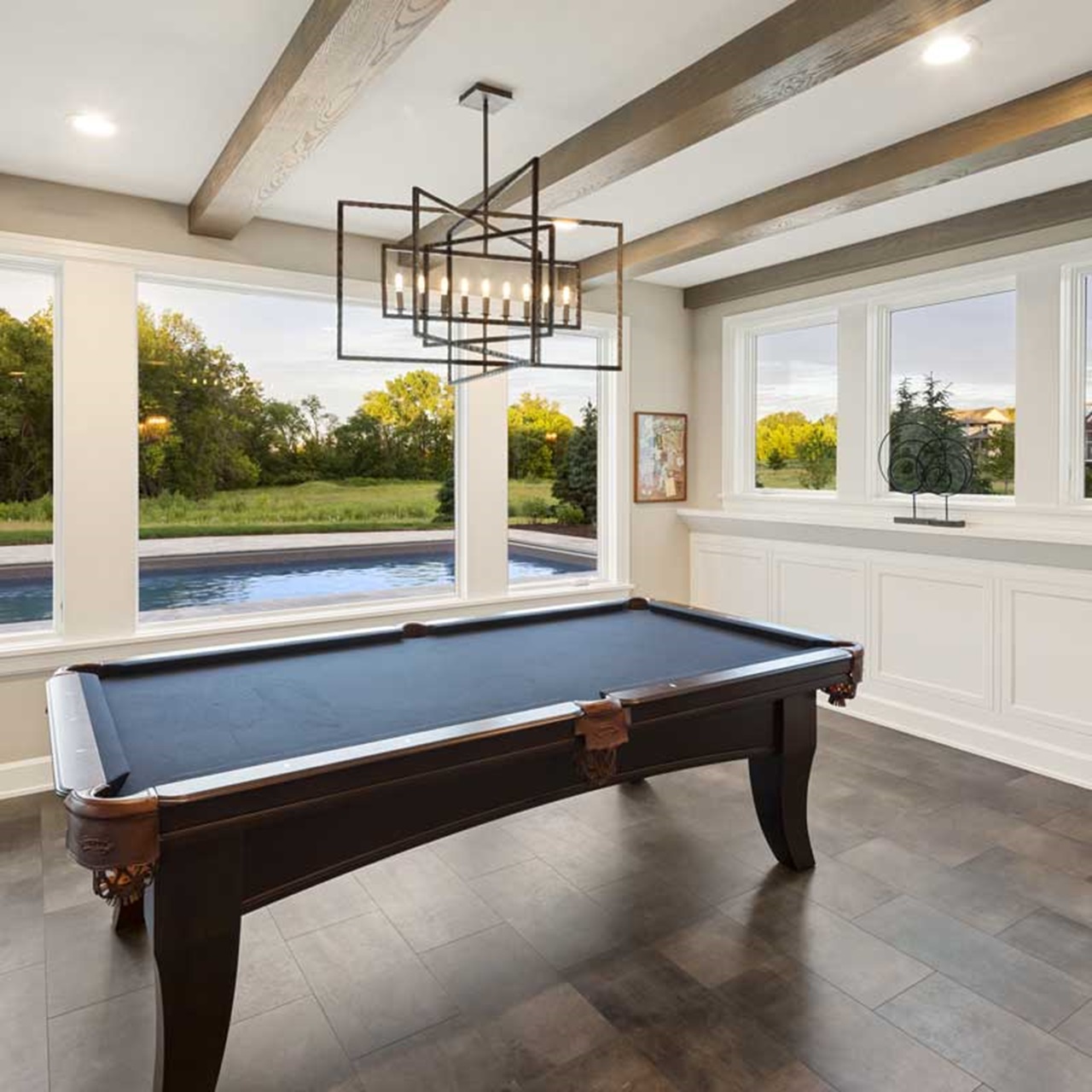 Game room with billiard table and view of pool through white elevate casement windows