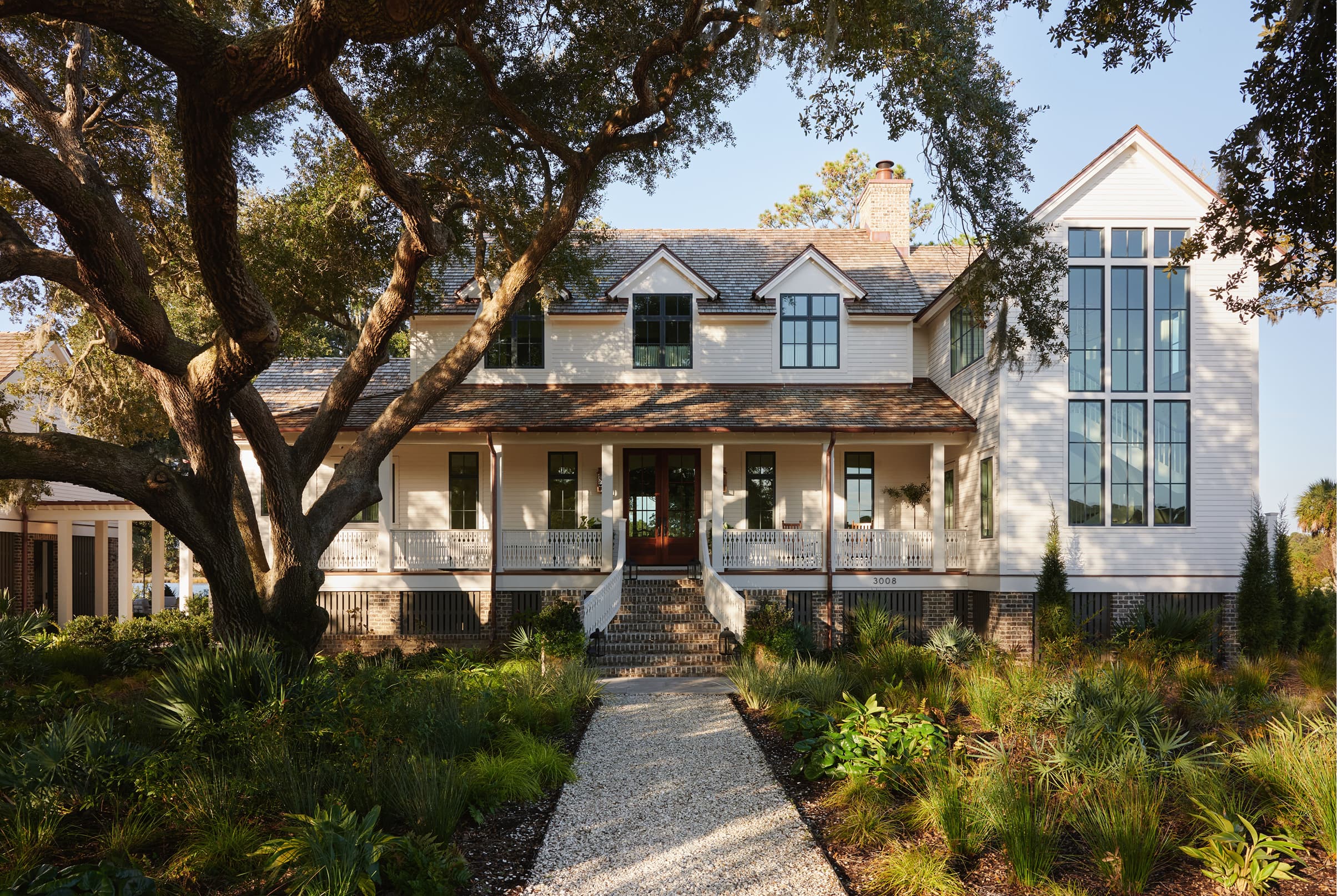 Large white lowcountry home exterior with a large tree in front with black Marvin Elevate Casement and Direct Glaze windows.